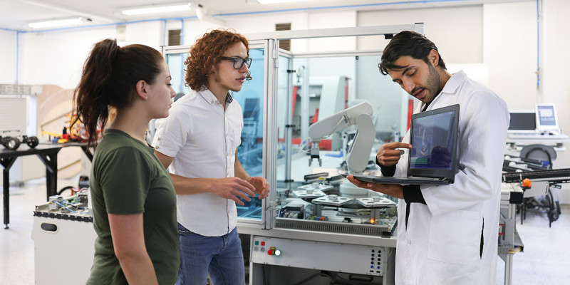 Two students in an engineering lab looking at a computer with a teacher